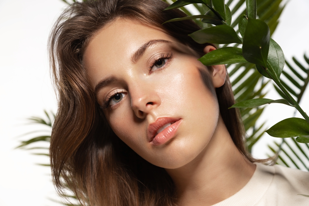 Piękna kobieta z idealną cerą i naturalnym makijażem trzymająca tropikalne liście